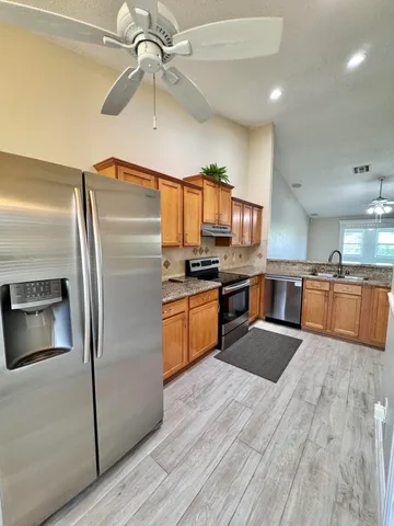 a kitchen with stainless steel appliances granite countertop a refrigerator a stove a sink a washer and dishwasher with wooden floor