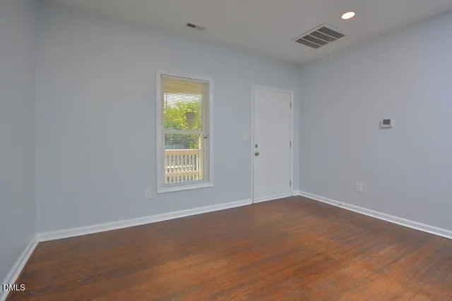 a view of an empty room with wooden floor and a window