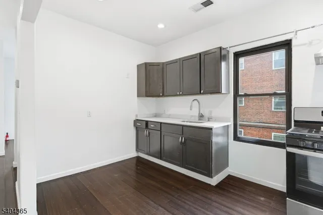 a kitchen with stainless steel appliances granite countertop a refrigerator a stove a sink and white cabinets with wooden floor