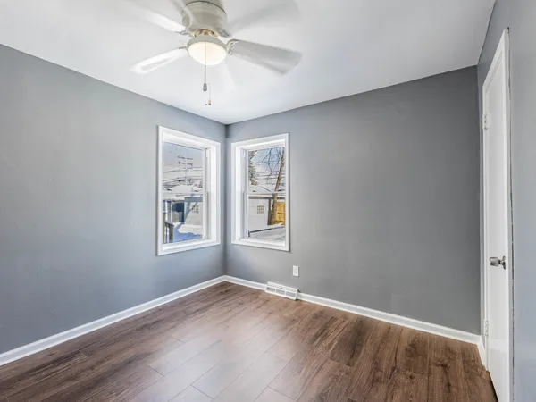 an empty room with wooden floor chandelier fan and windows