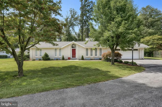 a view of a white house in front of a big yard with large trees