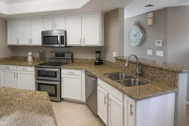 a kitchen with granite countertop a sink stainless steel appliances and white cabinets