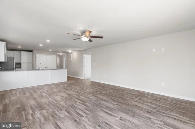 a view of an empty room with wooden floor and a kitchen
