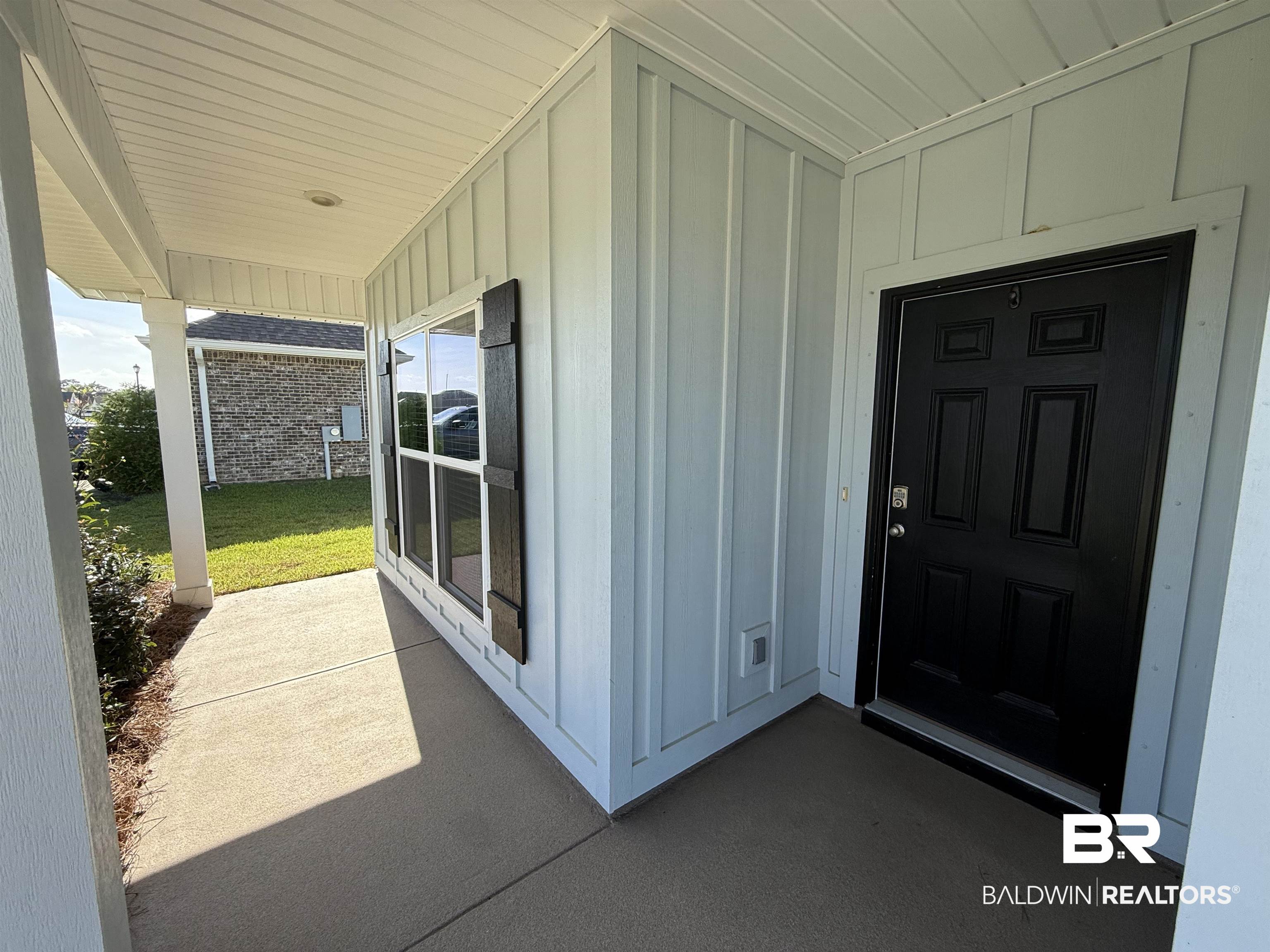 23247 Lieutenant Avenue Foley, AL 36535 - Photo 2 of 47 Covered porch entry featuring board and batten siding, a black paneled front door, and a window with dark decorative shutters