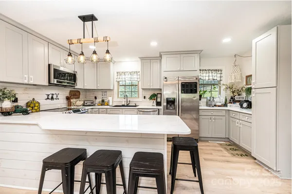 a kitchen with stainless steel appliances kitchen island granite countertop a table chairs refrigerator and microwave