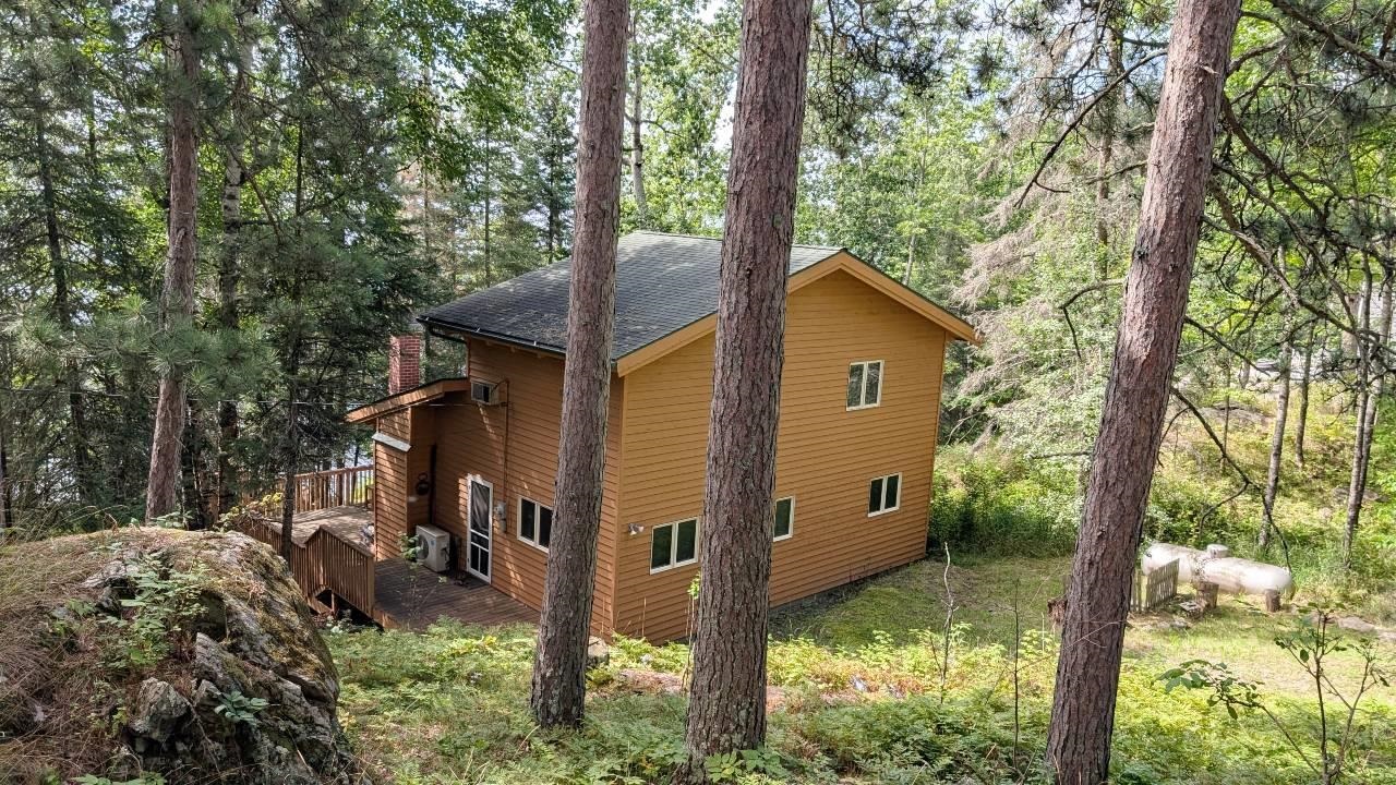View of home's exterior featuring a shingled roof, a deck, a wooded view, and a chimney