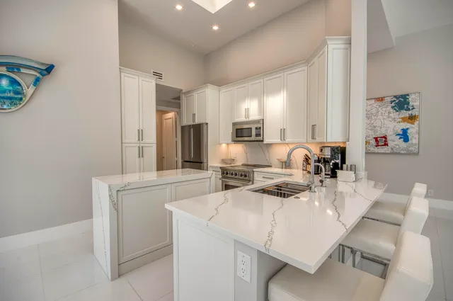 a kitchen with stainless steel appliances a sink a stove a refrigerator with white cabinets and wooden floor