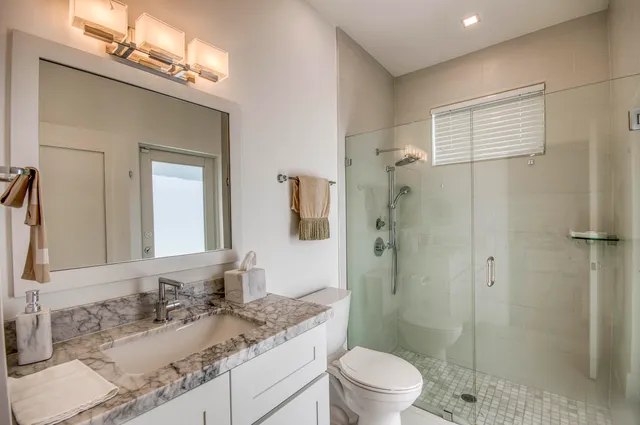 a bathroom with a granite countertop sink toilet a mirror a shower and vanity