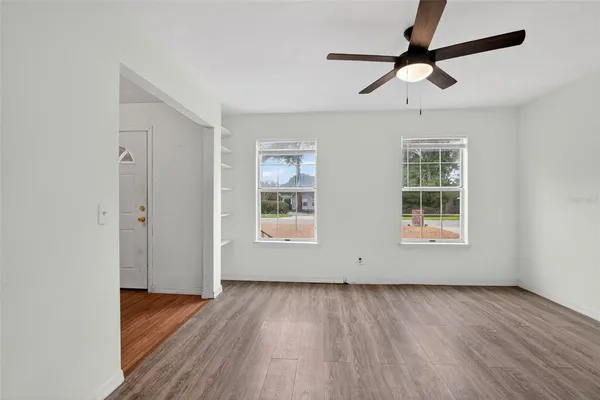 an empty room with wooden floor ceiling fan and windows