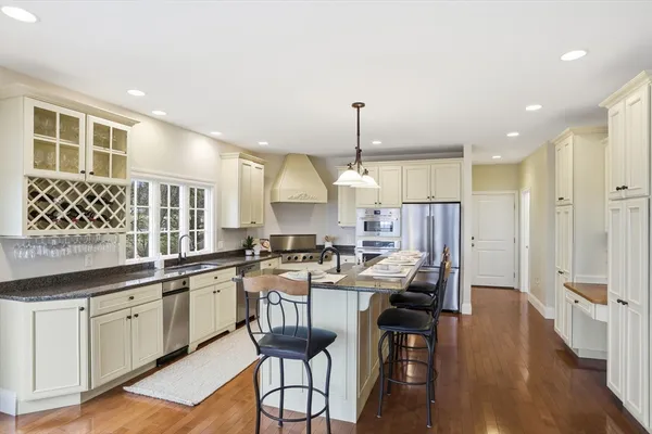 a open kitchen with granite countertop a stove a sink a dining table and chairs with wooden floor