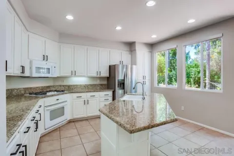 a kitchen with stainless steel appliances granite countertop a sink a stove a refrigerator and white cabinets with wooden floor