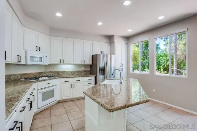 a kitchen with stainless steel appliances granite countertop a sink a stove a refrigerator and white cabinets with wooden floor