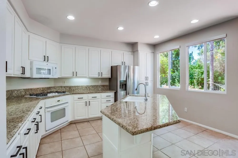 5423 Foxtail Loop Carlsbad, CA 92010 - Photo 11 of 53 a kitchen with stainless steel appliances granite countertop a sink a stove a refrigerator and white cabinets with wooden floor