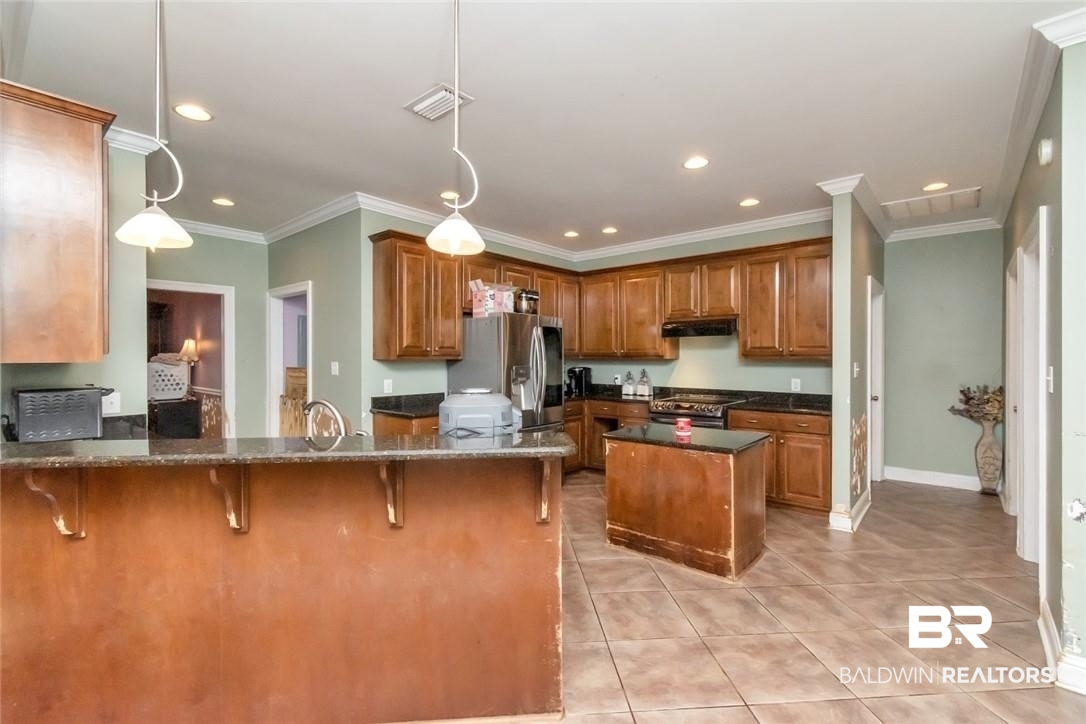 7170 Pierson Drive Mobile, AL 36619 - Photo 8 of 29 Kitchen featuring dark stone countertops, appliances with stainless steel finishes, decorative light fixtures, crown molding, and kitchen peninsula