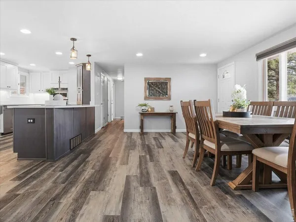 a dining hall with stainless steel appliances kitchen island granite countertop a table chairs and a wooden floor