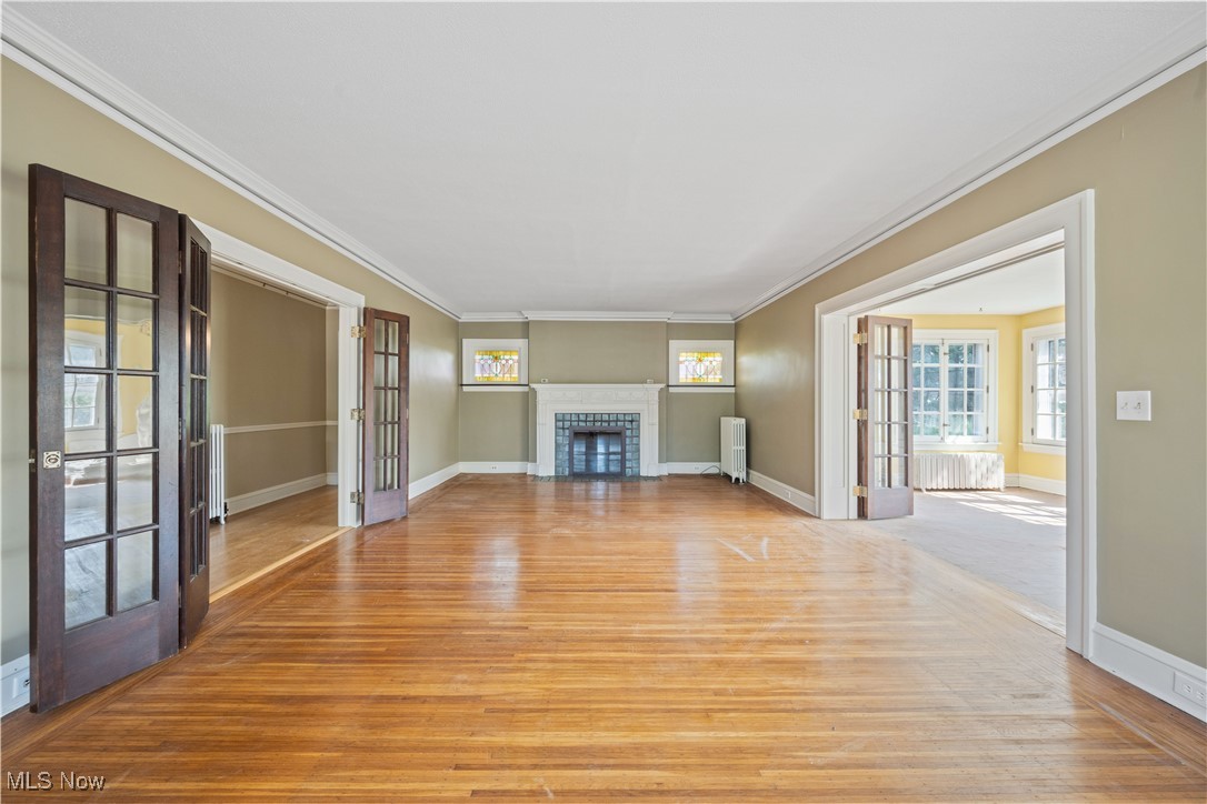 24510 Lake Road Bay Village, OH 44140 - Photo 8 of 45 Unfurnished living room featuring french doors, ornamental molding, light wood finished floors, a fireplace with flush hearth, and radiator