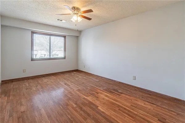an empty room with wooden floor chandelier fan and windows
