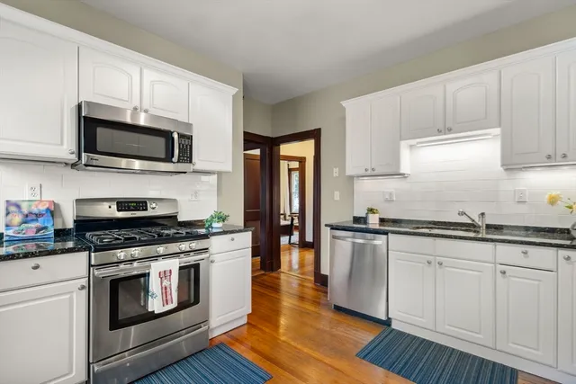 a kitchen with stainless steel appliances granite countertop grey cabinets a sink a stove a microwave and wooden floors