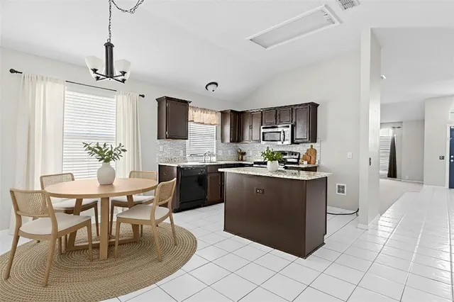 a kitchen with stainless steel appliances granite countertop a stove top oven a refrigerator a sink and a dining table with white cabinets