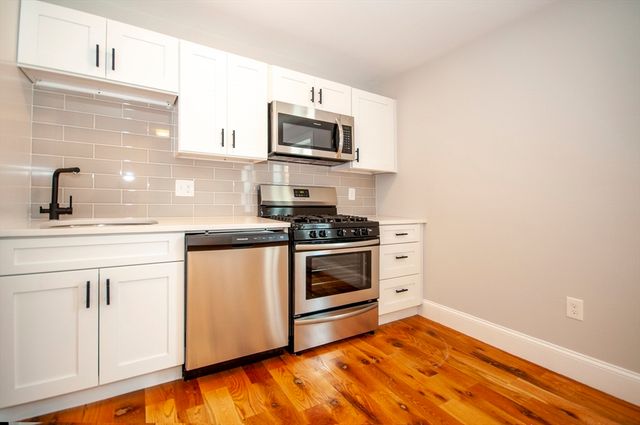 a kitchen with granite countertop white cabinets stainless steel appliances and wooden floor