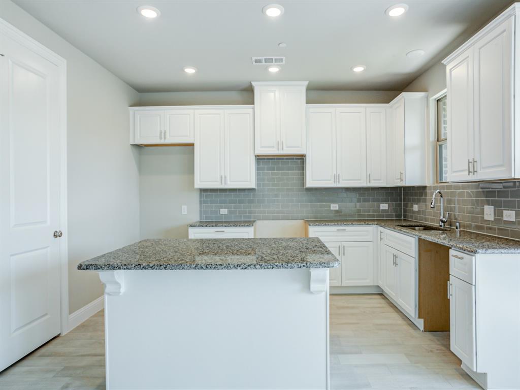 a kitchen with kitchen island granite countertop a sink and white cabinets