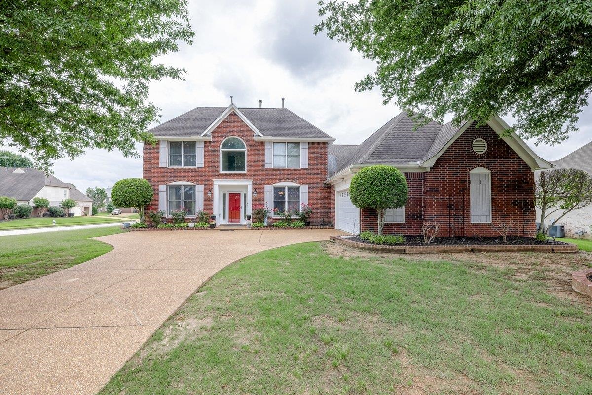 Traditional brick residence featuring a prominent red entry door, white louvered shutters, and a curved driveway