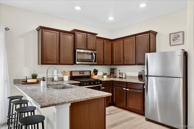 a kitchen with granite countertop a refrigerator a sink a stove a microwave and wooden cabinets