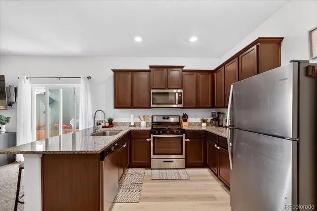 a kitchen with granite countertop a refrigerator a sink a stove a microwave and wooden cabinets