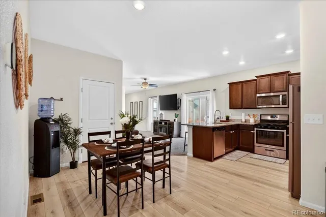 a kitchen with stainless steel appliances kitchen island granite countertop a refrigerator a stove a sink a dining table and chairs with wooden floor