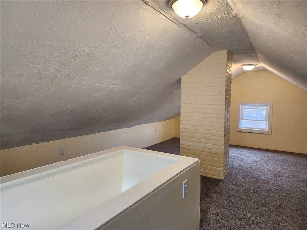 17814 Crestland Road Cleveland, OH 44119 - Photo 29 of 49 Additional living space with brick wall, dark carpet, vaulted ceiling, and a textured ceiling