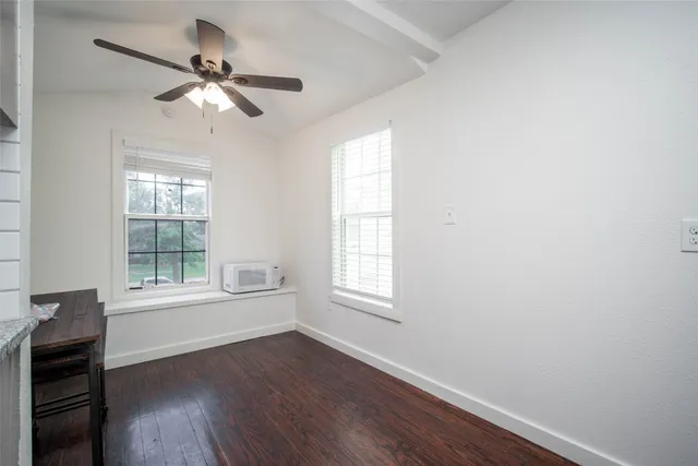 an empty room with wooden floor fan and windows