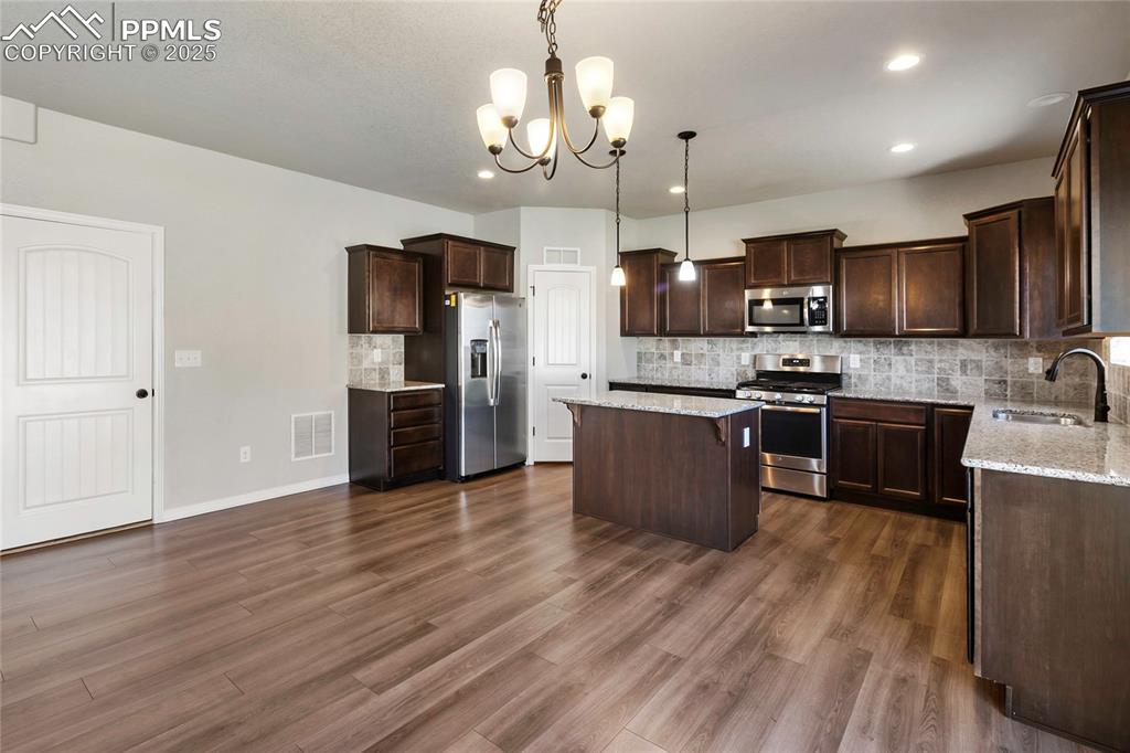 10858 Traders Parkway Fountain, CO 80817 - Photo 8 of 38 a kitchen with stainless steel appliances kitchen island granite countertop a stove top oven a sink dishwasher a refrigerator and a dining table with wooden floor