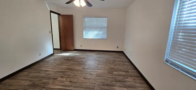 an empty room with wooden floor chandelier fan and windows