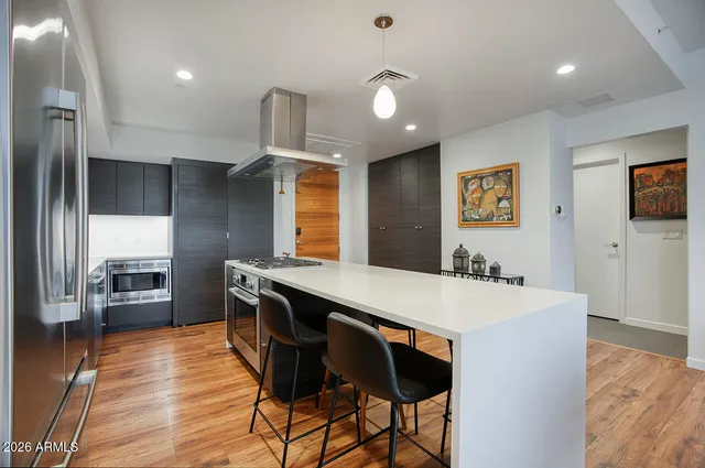 a kitchen with stainless steel appliances kitchen island granite countertop a refrigerator a stove and a wooden floors