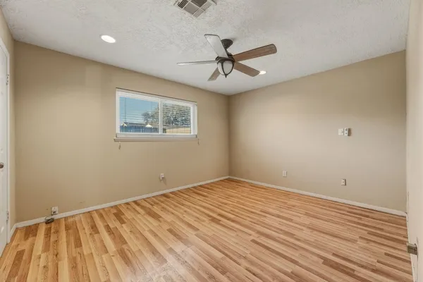 a view of an empty room with wooden floor and a ceiling fan