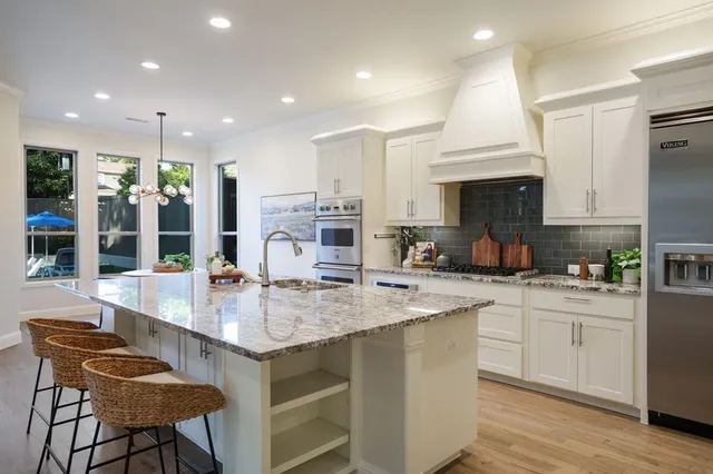 a kitchen with stainless steel appliances granite countertop a sink a stove a refrigerator and a dining table with wooden floor