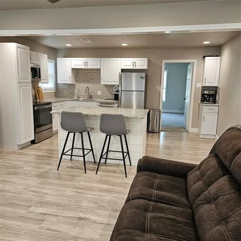 a living room with stainless steel appliances kitchen island granite countertop furniture and a wooden floor