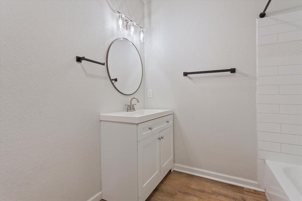 3109 North 20th Street Waco, TX 76708 - Photo 12 of 24 Vanity featuring white shaker-style cabinetry with silver hardware, a white countertop with integrated sink, and a circular mirror with a black frame