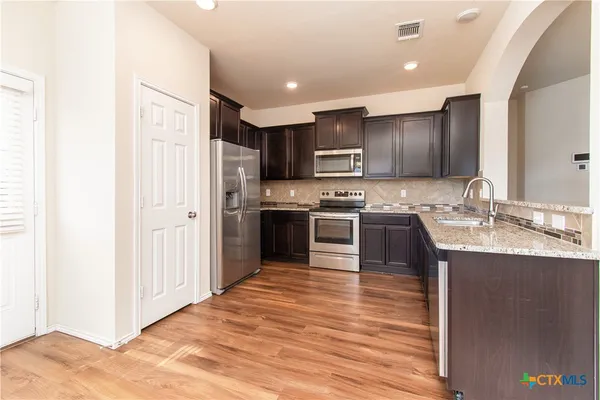 a kitchen with stainless steel appliances granite countertop a stove top oven a sink and a refrigerator