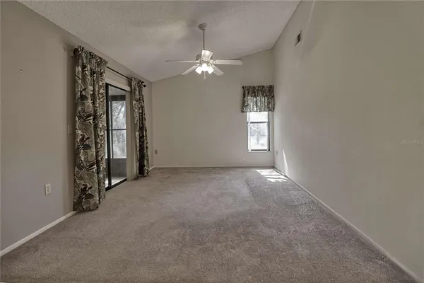 an empty room with chandelier fan and windows