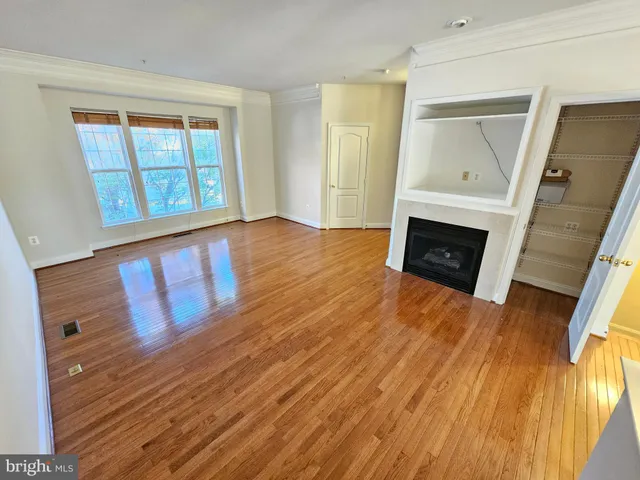 a view of an empty room with wooden floor fireplace and a window