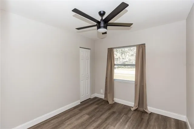 an empty room with wooden floor ceiling fan and windows