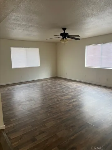 an empty room with wooden floor a ceiling fan and windows