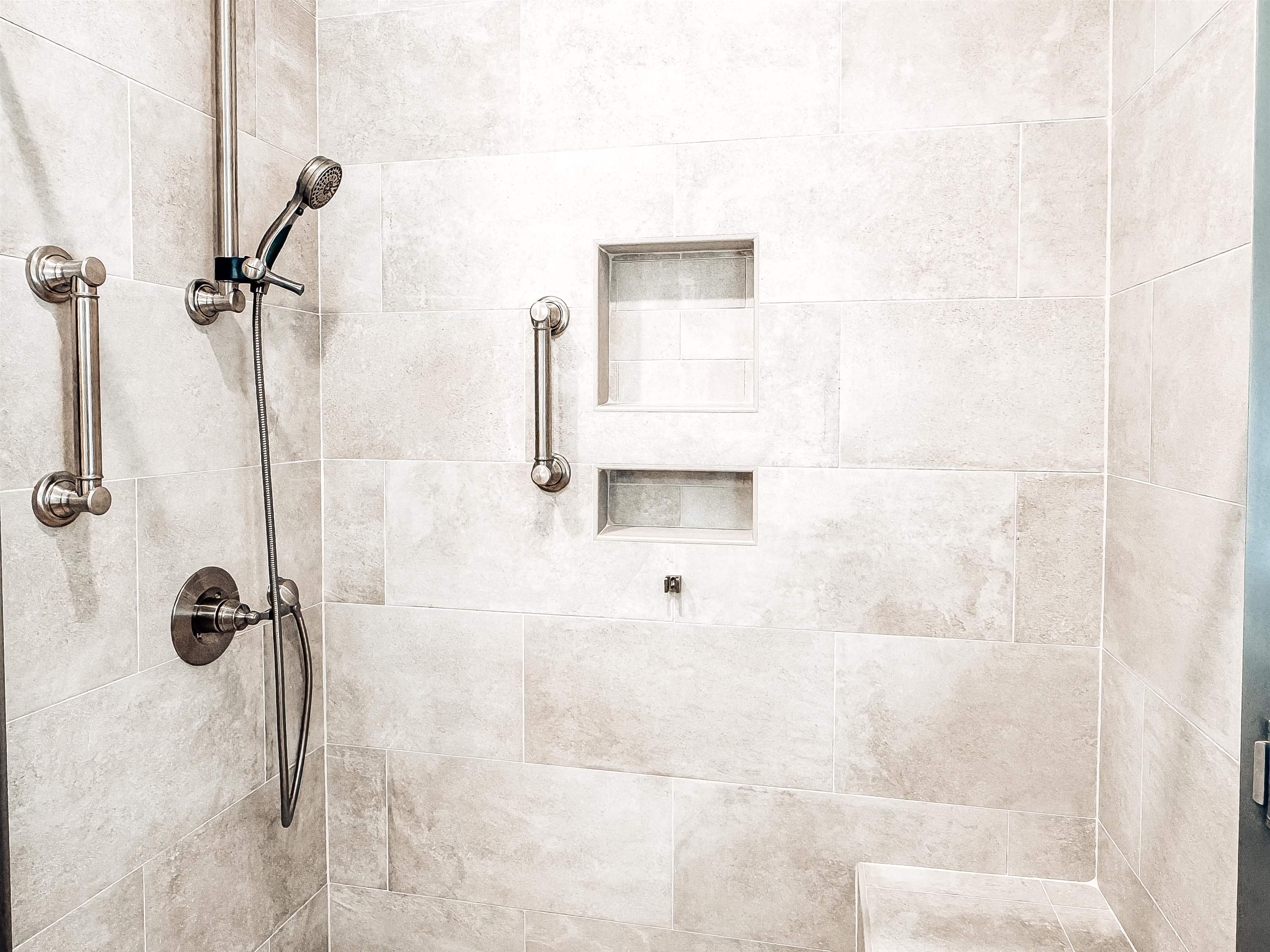 832 South Tree Drive Collierville, TN 38017 - Photo 21 of 40 Tiled shower enclosure featuring light-toned large format tile, brushed nickel shower fixtures with a handheld spray, integrated wall niches, built-in seating, and grab bars