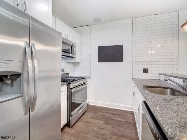 a kitchen with stainless steel appliances granite countertop a refrigerator a stove and a sink with wooden floor