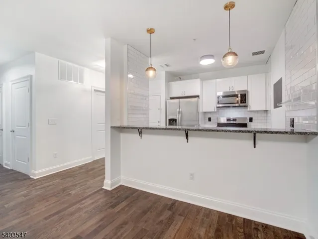 a view of a kitchen with stainless steel appliances granite countertop a sink a refrigerator a stove a microwave and a wooden floors