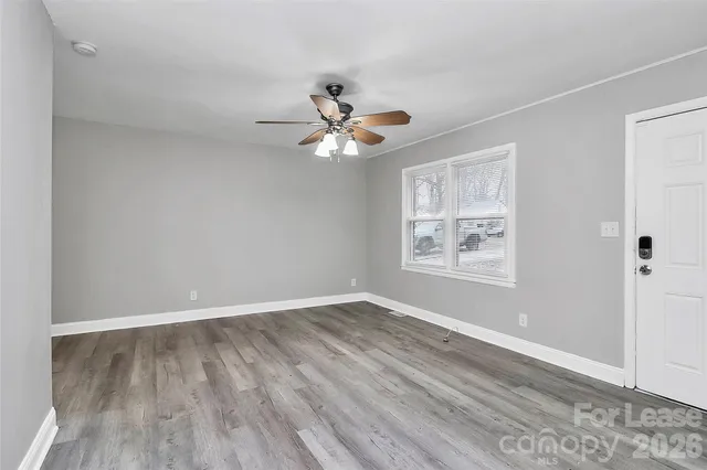an empty room with wooden floor chandelier fan and windows