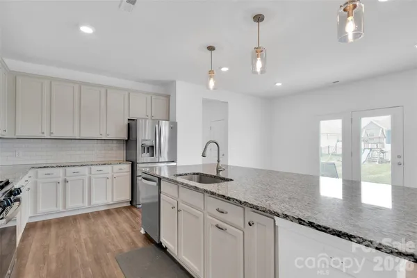 a kitchen with stainless steel appliances granite countertop a sink dishwasher and white cabinets with wooden floor