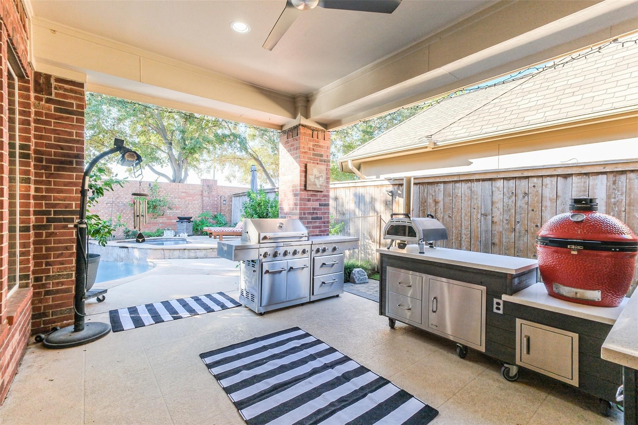 11413 Gallant Ridge Lane Houston, TX 77082 - Photo 48 of 50 This photo showcases a spacious outdoor patio with a modern barbecue area, including a grill and smoker. It features brick accents, a ceiling fan, and a view of a pool, making it ideal for entertaining and relaxation. Personal property not included with sale
