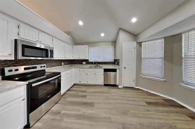 a large kitchen with granite countertop a stove top oven a sink dishwasher a refrigerator and white cabinets with wooden floor